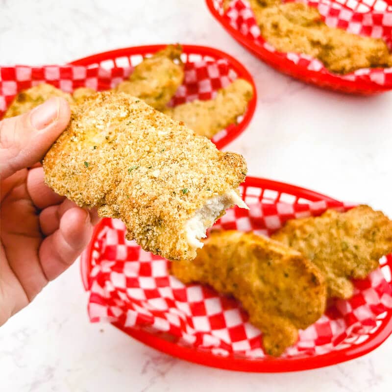 A hand holding up a chicken tender with a bit taken out of it.