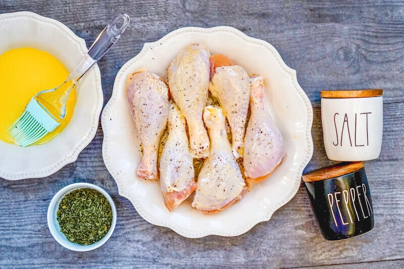 A plate of raw drumsticks coated with butter and seasonings.