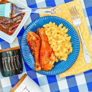 A blue and white checked placemat topped with a blue plate of drumsticks coated with barbecue sauce.