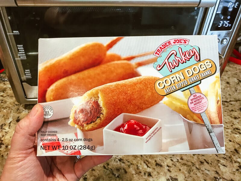 A box of Trader Joe's Turkey Corn Dogs held up in front of an air fryer.