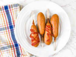 A plaid towel next to a plate of air fried corn dogs.