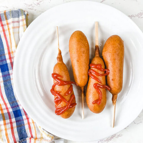 A plaid towel next to a plate of air fried corn dogs.