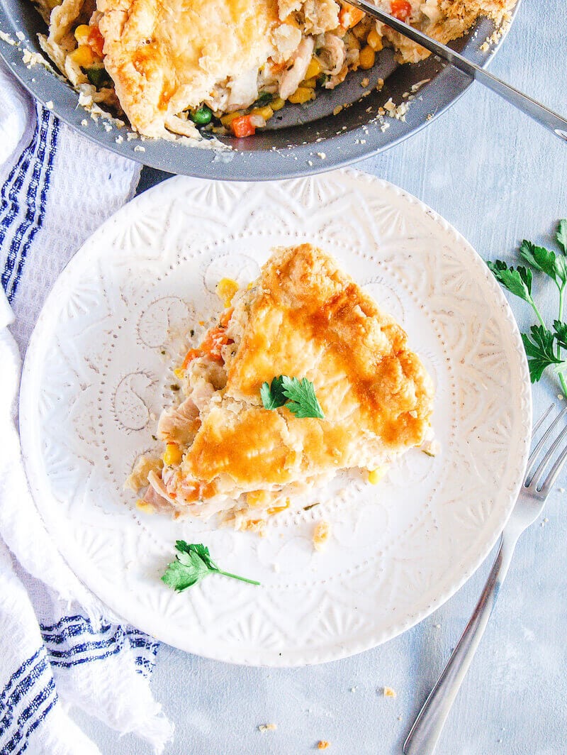 A white plate with a slice of pot pie topped with fresh herbs.