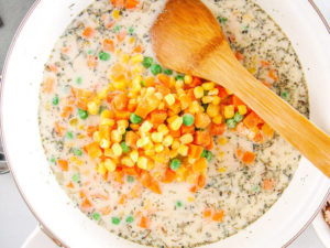 A pot with a roux and frozen vegetables on top.