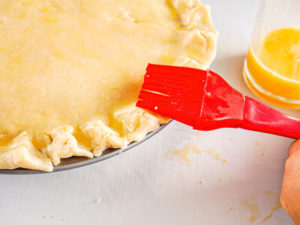 A pastry brush brushing egg wash onto pie crust.