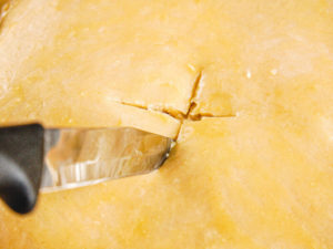 A knife cutting an X in the center of a pot pie.