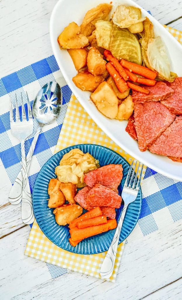 A blue plate of corned beef, potatoes, carrots, and cabbage with a fork next to it.
