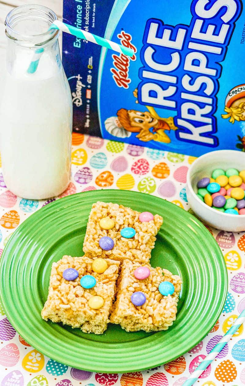 Close up of Rice Krispie treats on a green plate with cereal box in the background.