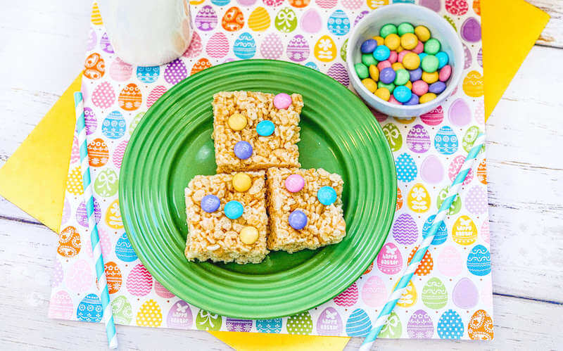 Green plate with three Easter themed Rice Krispie treats next to a bottle of milk.