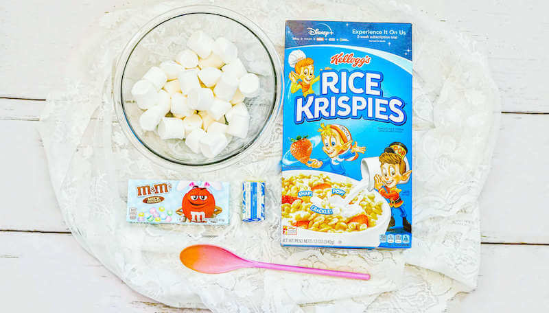 A round white platter with a box of Rice Krispie treats, marshmallows, and Easter M&Ms.