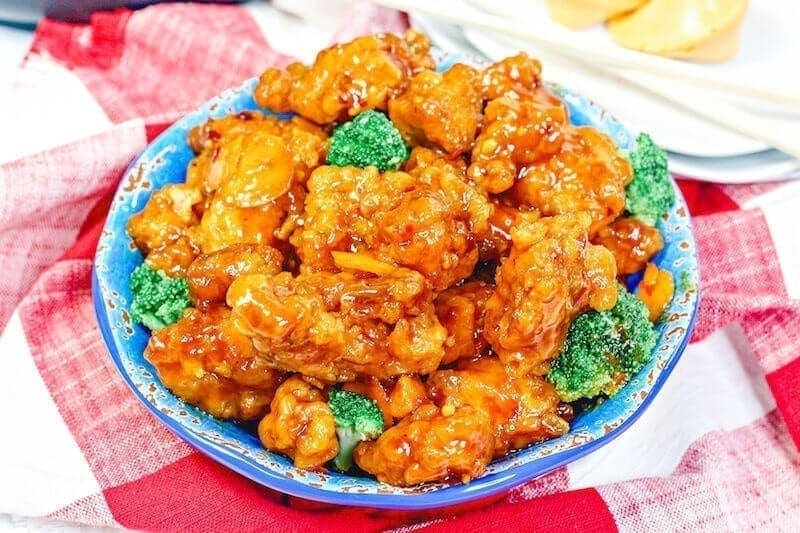 A full bowl of orange chicken on top of a red checkered tablecloth.