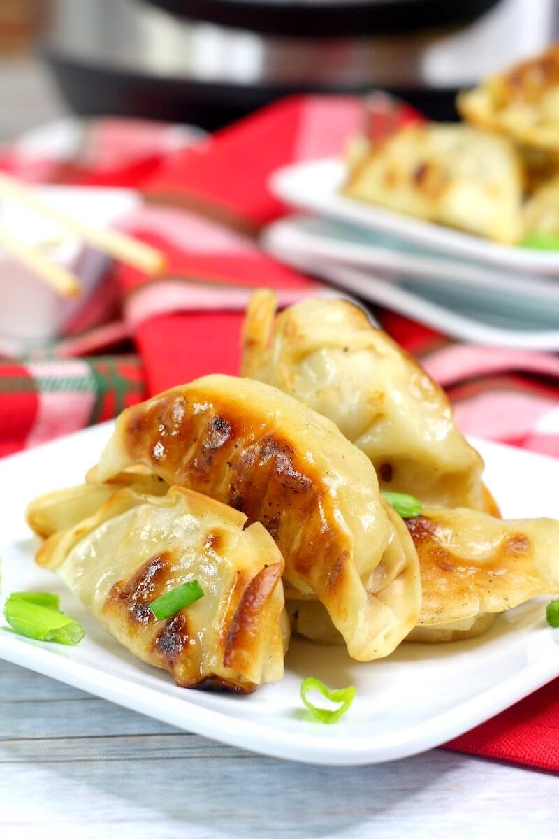 Close up of pot stickers on a white plate with red cloth napkins in the background.