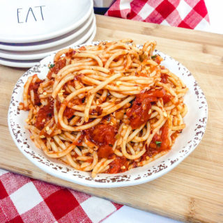 A cutting board with a plate piled high with spaghetti.