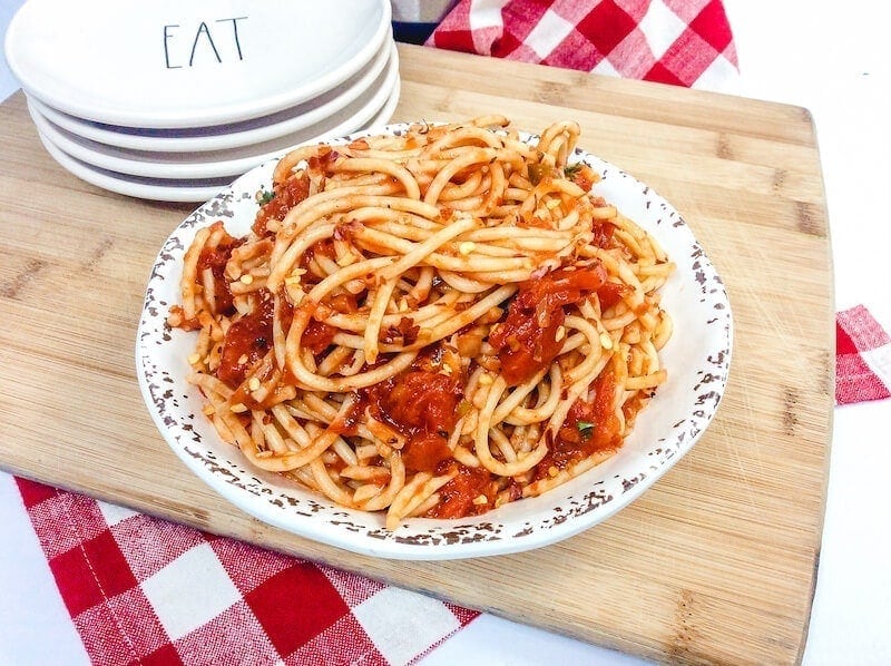 A cutting board with a plate piled high with spaghetti.