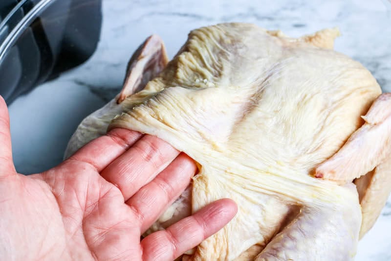 Skin being lifted up on a raw whole chicken