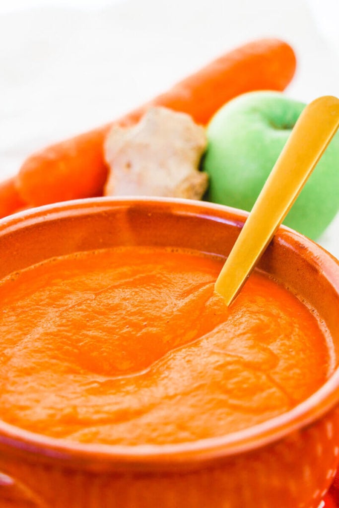 A bowl of carrot soup with a gold spoon sticking out of the bowl.