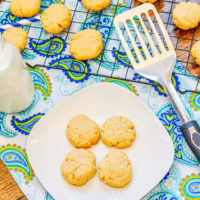 A blue and green place mat with a white plate of shortbread cookies, bottle of milk, and metal spatula on top.