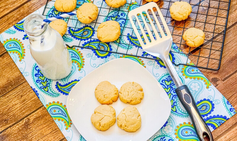 A blue and green place mat with a white plate of shortbread cookies, bottle of milk, and metal spatula on top.