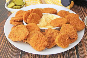 A white dish filled with golden brown air fryer pickles.