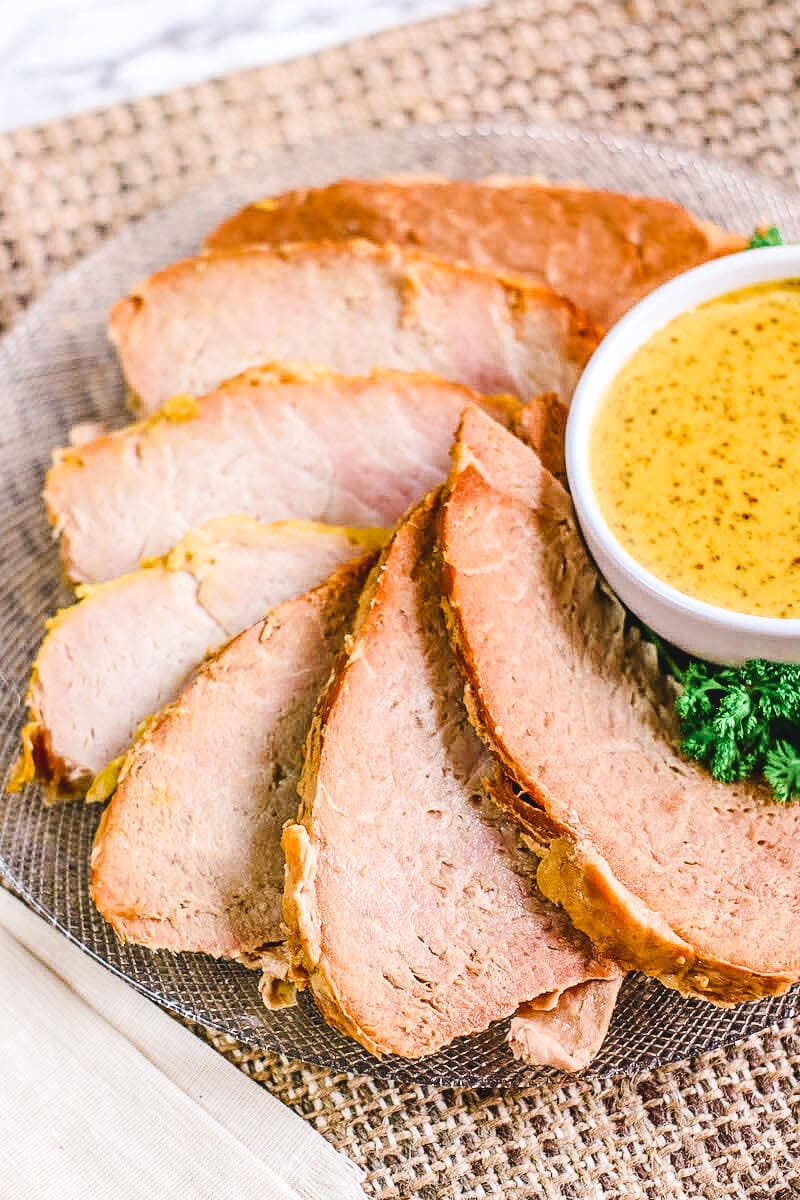 Slices of ham on a glass platter next to a small white bowl of mustard.