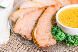 Close up of three slices of ham next to a small bowl of mustard.
