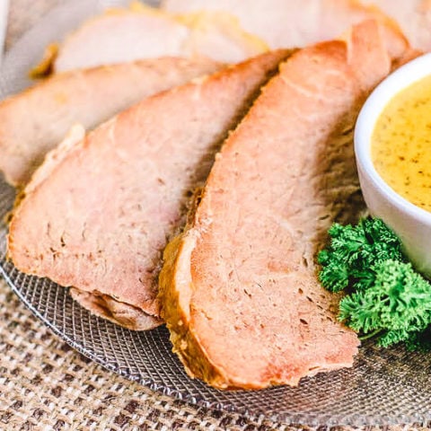 Close up of three slices of ham next to a small bowl of mustard.