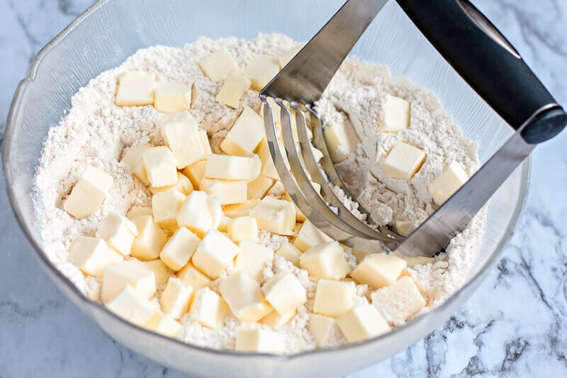 A pastry cutter on top of a bowl of flour and cubed butter.