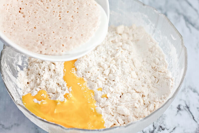 Eggs and yeast being poured into bowl of flour.