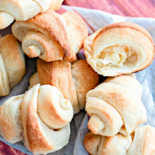 A pile of freshly baked crescent rolls on a blue tea towel.