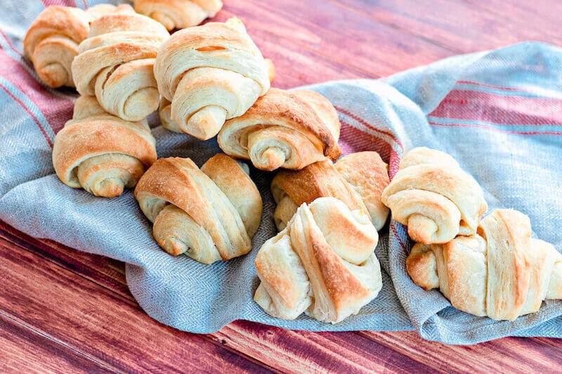 A blue towel with a batch of homemade crescent rolls stacked on top.