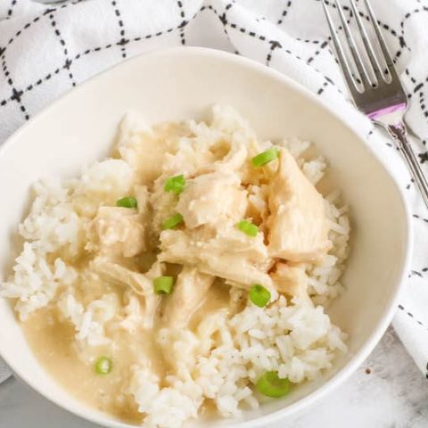 Close up of chicken and gravy served over rice in a white bowl.