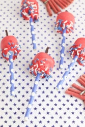 Marshmallow pops decorated to look like 4th of July firecrackers on a blue polka dot background.
