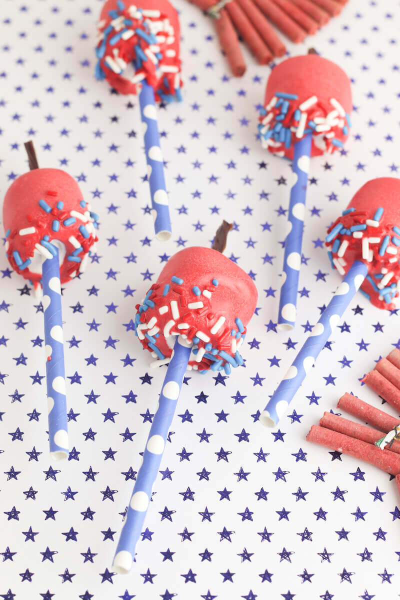 Marshmallow pops decorated to look like 4th of July firecrackers on a blue polka dot background. 