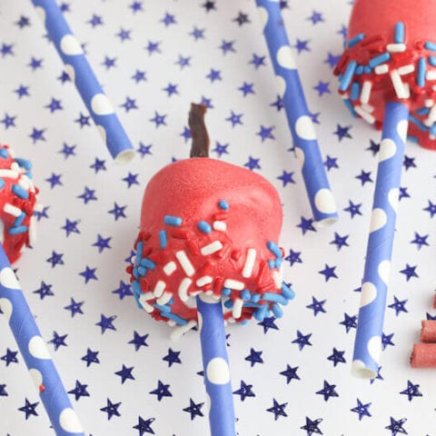 Three red candy coated marshmallow pops decorated to look like firecrackers.
