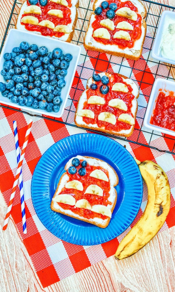 A red and white checkered placemat topped with a blue plate holding a piece of toast decorated to look like an American Flag.