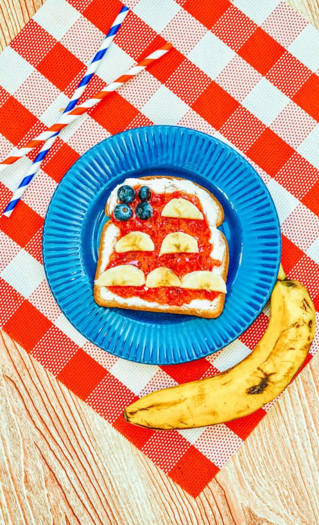 Toast decorated to look like an American Flag on a blue plate next to a banana.