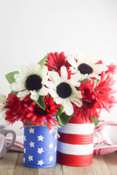 Two diy vases painted to look like the American flag and filled with white and red flowers.
