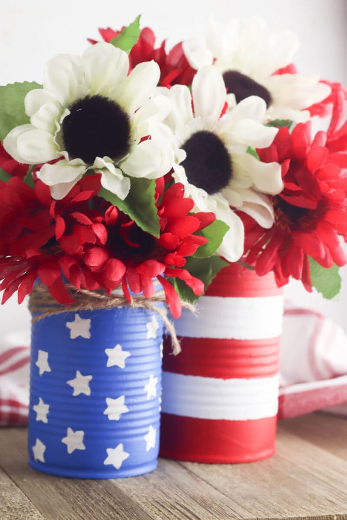 Two diy vases, one blue with white stars and one with red and white stripes, filled with flowers.