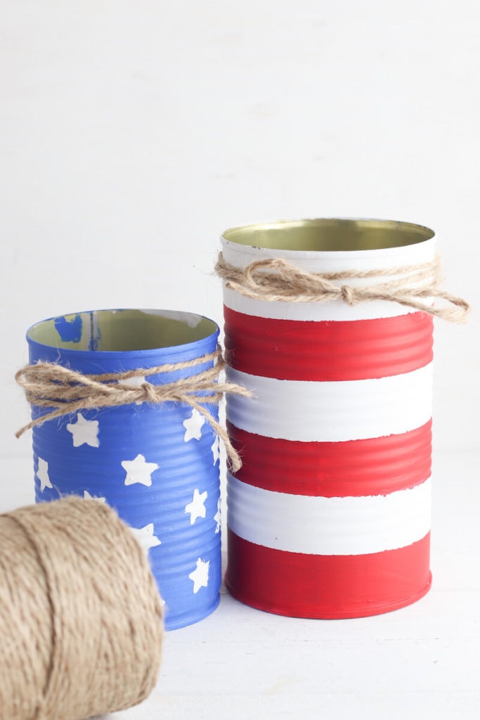 Two tin cans painted to look like the american flag with twine wrapped around the top of them.