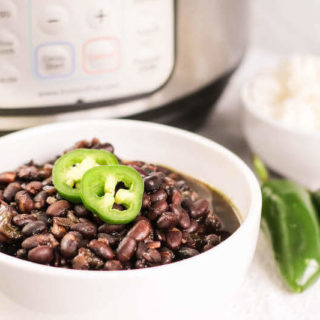 A white bowl of cuban black beans toped with sliced jalapeños.