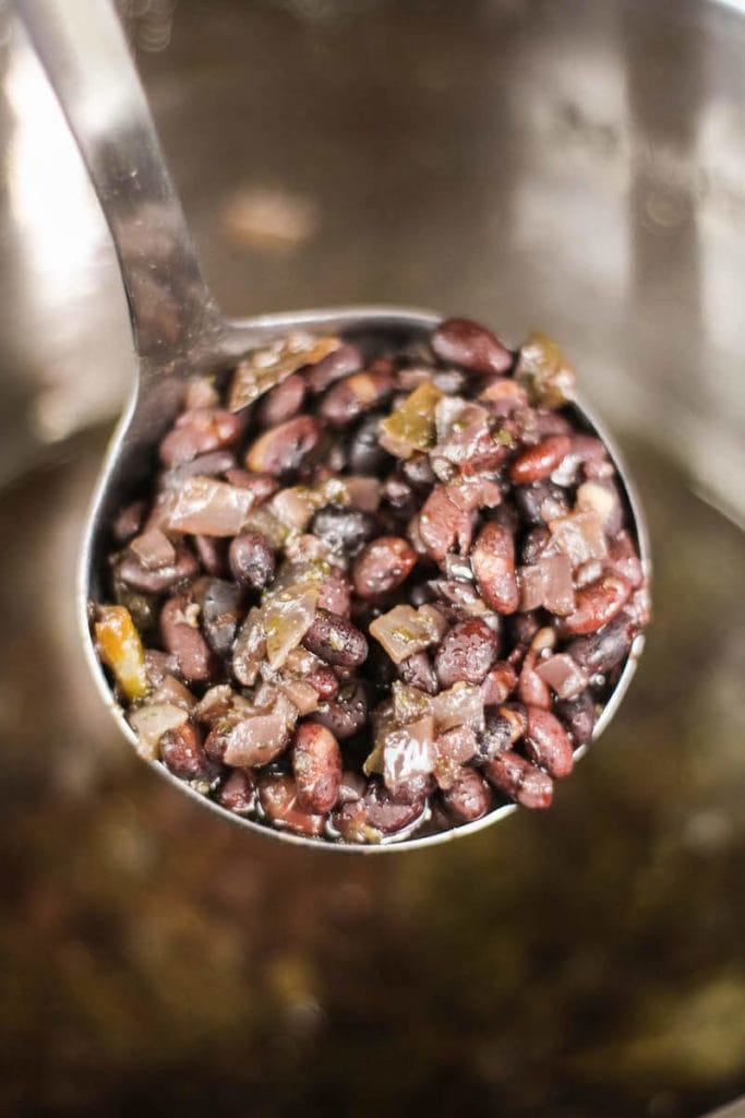 A ladle full of cuban black beans over the inside of the inside of the instant pot with cooked beans inside.