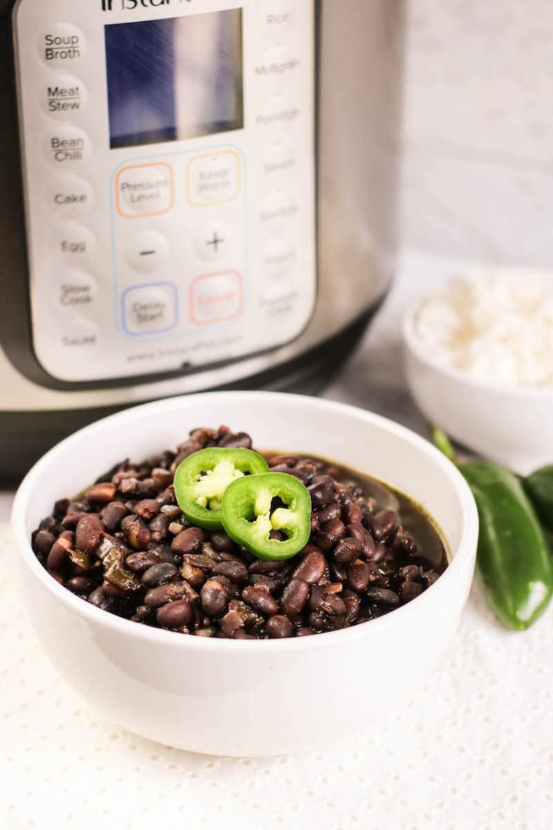 A white bowl filled with cuban black beans in front of an instant pot and and next a bowl of white rice.