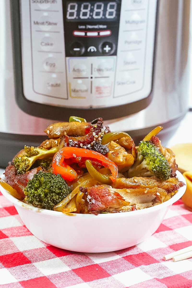 A white bowl filled with honey garlic chicken in front of an instant pot.