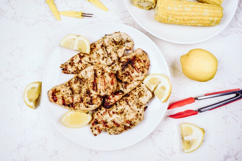 A plate full of grilled chicken with lemon wedges around it.