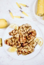 A white plate of grilled chicken and lemon wedges.
