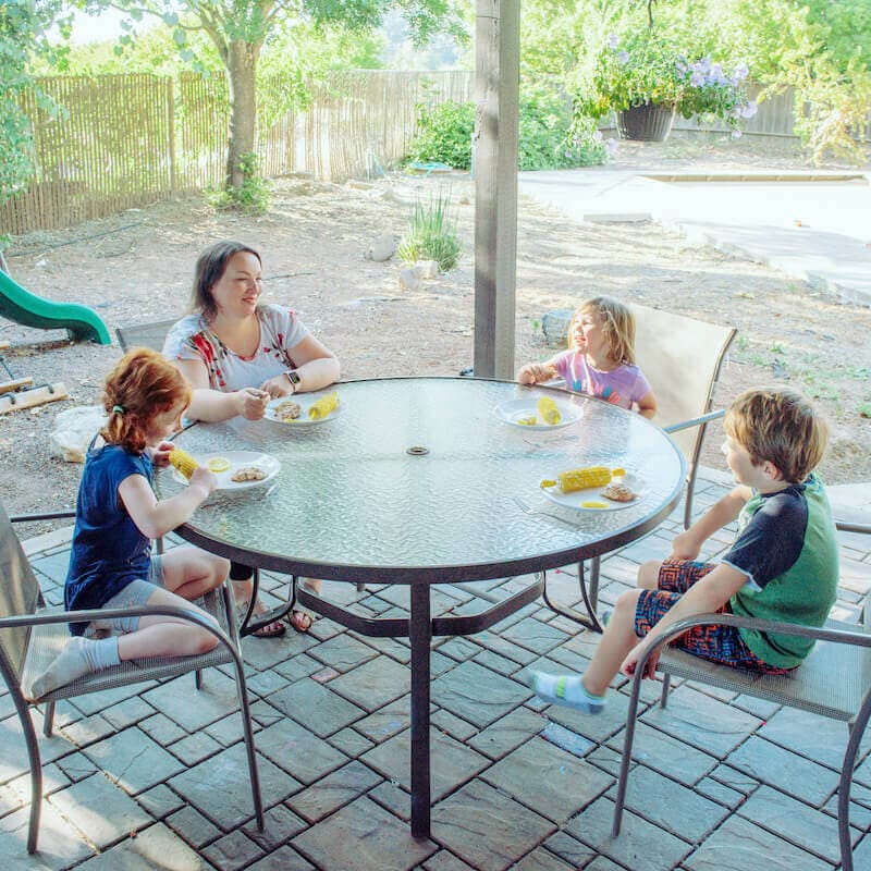 A mom and three kids sitting around a glass table outside.