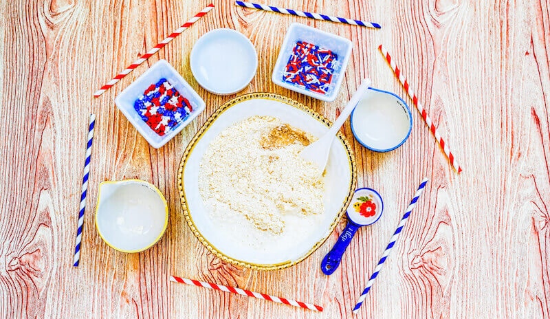 A bowl of butter and sugar mixed together next to two small bowls of milk and vanilla extract.