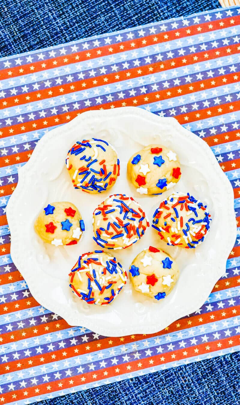A red white and blue striped placemat topped with a white plate of edible sugar cookie dough.