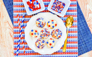 A white plate filled with balls of sugar cookie dough topped with patriotic sprinkles.