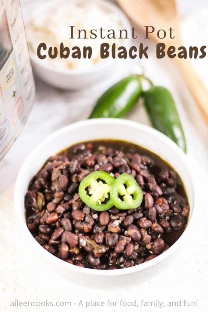 A bowl of black beans topped with two slices of jalalpeno and the words "instant pot cuban black beans" in brown lettering.